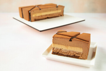 Sliced ​​piece of mousse chocolate cake on the plate with a square half cake in the background - concept of a festive serving dessert in a cafe - close-up