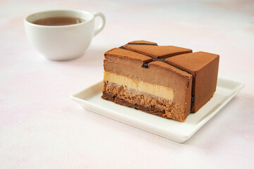 Traditional piece of delicious mousse chocolate cake on a white square plate with a cup of hot tea - dessert in a cafe