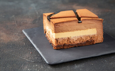 A piece of mousse chocolate cake with a beautiful cutting on a black plate on a dark background - close-up