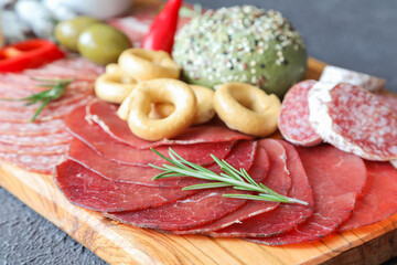 Italian bresaola sliced on a meat board with rosemary, taralli, olives and red pepper in the background, and a sesame bun - red wine appetizer