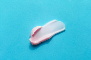 Textured smear of pink creamy foam isolated on blue background. Creme, lotion, facial mask. Beauty selfcare