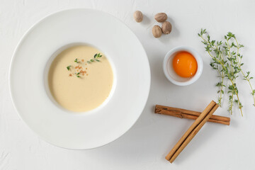 Traditional Italian soup in a large white plate with fields and ingredients - egg yolk, cinnamon sticks, thyme, and nutmeg