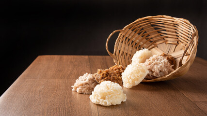 Cocada, Coconut candy from Brazil, white and brown cocadas fallen from a straw basket on wooden surface, black background, selective focus.