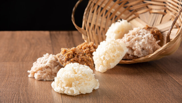 Cocada, Coconut candy from Brazil, white and brown cocadas fallen from a straw basket on wooden surface, black background, selective focus.