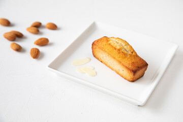 Single financier cake on a white square plate with almonds and almond shavings - a concept and the main ingredient for making French pastries