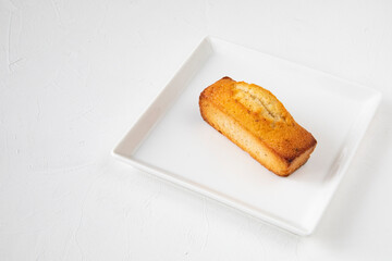 Single French pastry on a white square plate on a white table - traditional financier cake