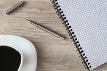 White cup of strong black coffee with metal pen and notepad on wooden surface close up