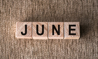 Fototapeta premium JUNE word written on wooden blocks on a brown background.