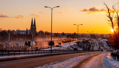 Olsztyn sunset winter - Artyrelyjska street, a freight train raises clouds of snow while driving, in the distance you can see the garrison church
