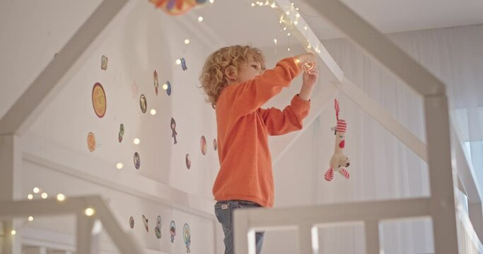 Cute boy examining fairy lights on canopy bed