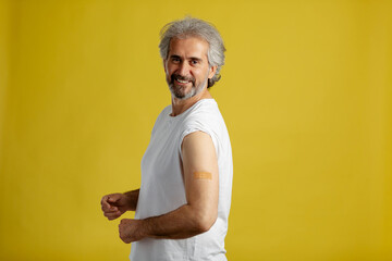 Happy vaccinated mature man showing shoulder with plaster bandage after Covid-19 vaccine injection.