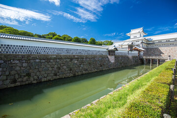 Kanazawa Castle, white walled Japanese fortress battlements. Entrance to Kenrokuen Garden. Bright blue sky, castle moat reflection. Ishikawa, Japan.