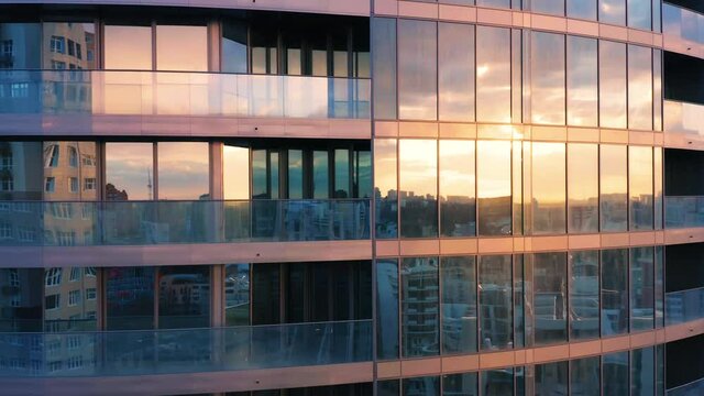 Aerial view of glass skyscraper with city reflection in windows at sunset.