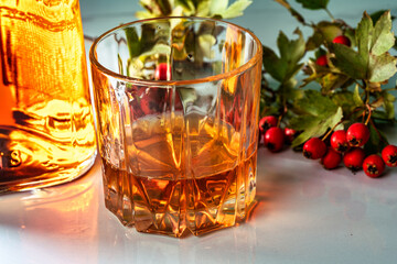 glass of whiskey with ice next to a bottle and a branch of viburnum