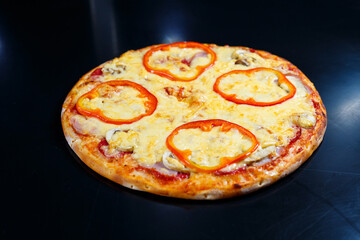 Hot delicious homemade American pizza with red pepper and meat with a thick crust on a black table