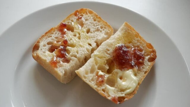 Two slices of white bread with butter and jam on a white plate. White background. Camera motion