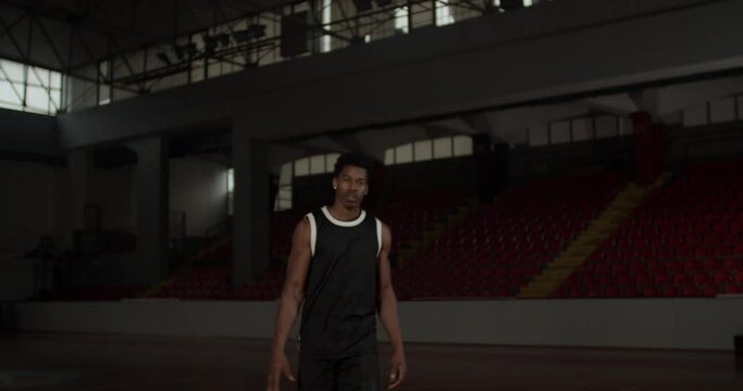 Video portrait of a basketball player bouncing a ball. African american man in uniform posing inside sports hall