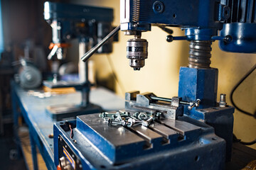 Metal chrome bolts and nuts lie on the drilling machine at the workplace