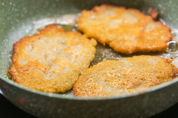 Potato pancakes on ceramic green frying pan closeup. Selective focus.