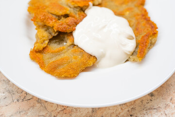 Potato pancakes with sour cream on ceramic white plate close up. Poor country cheap food.