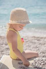 Cute little girl is playing with pebbles on the beautiful beach. Child relaxing on beach resort.