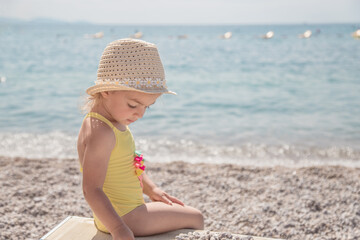 Cute little girl is playing with pebbles on the beautiful beach. Child relaxing on beach resort.