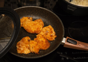frying pieces of breaded chicken in a frying pan. electric stove.
