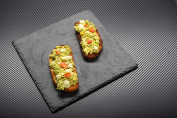 Two sandwiches with avocado, tomato and egg. Sandwiches on a black tray.