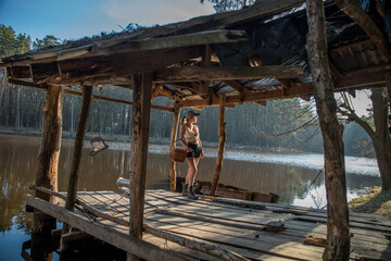 A girl with a basket in a wooden building on the lake in the warm evening light of the setting sun.