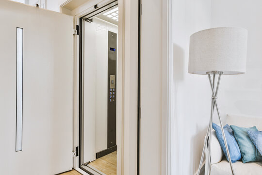 Opened metal door of elevator located near sofa and lamp in modern flat