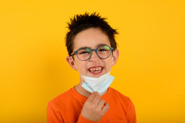 Child is happy to remove the face mask for covid-19coronavirus. yellow background
