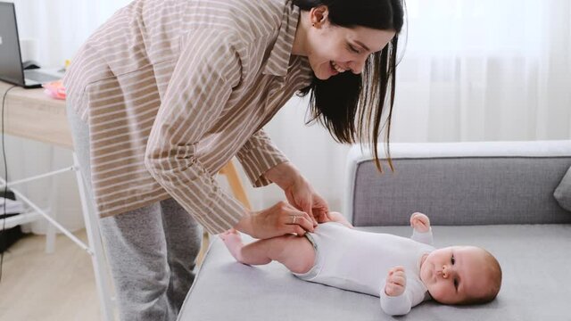 Dressing up infant baby at home on the coach before walk, Having fun with mother during morning routine. changing body. Caucasian infant dress up after bathing by his mommy.