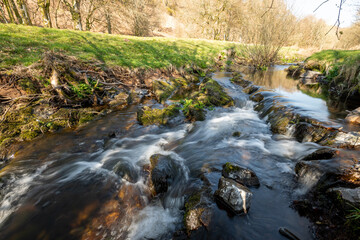 Naklejka na ściany i meble Long exposure of the Weir Water river flowing through the valley at Robbers Bridge in Exmoor National Park