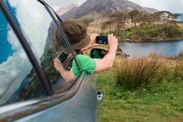 Male driver taking picture from a car window on his smart phone of Twelve pines island, county Galway, Connemara region, Ireland. Travel and tourism concept.