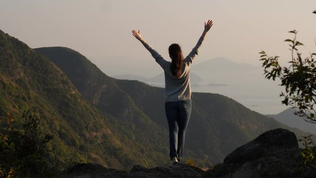 Tourist woman stay at height with hands stretched out, enjoy forested mountains and South China Sea view from Lantau island. Full length shot from back
