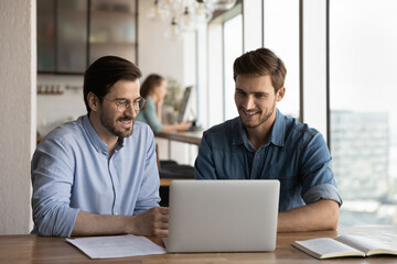Smiling male employees colleagues work together brainstorm using modern computer gadget at meeting...
