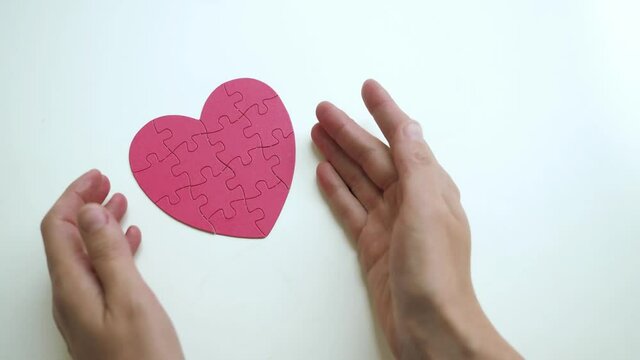 Top view of woman's hands open hided small red heart shaped jigsaw from paper blocks puzzle on white table background