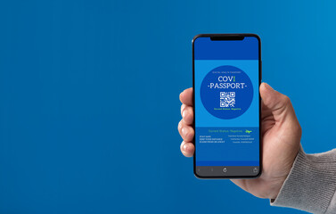 phone in hand with covid passport on screen, with blue background, gray clothes.