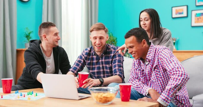 Happy Diverse Friends Watching Funny Video, Laughing At Joke, Using Laptop, Having Fun Together, Sitting On Couch, Looking At Computer Screen, Students Colleagues Working On Online Project