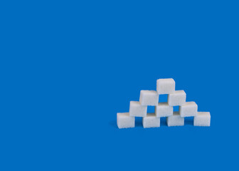 A pyramid of sugar cubes on a blue background. Close-up. Copy space.