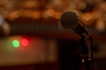 A silver metal microphone on a stand. The round ball style mic is a classic for concerts and evening music sessions. The electronic equipment has an on and off button.The background is orange bokeh.