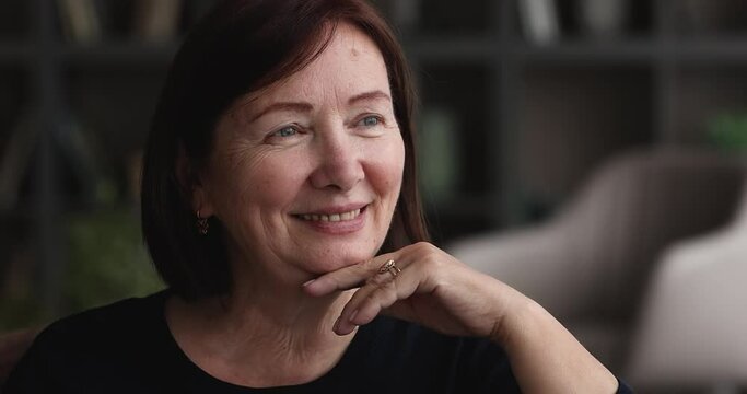Close up portrait smiling caucasian elderly woman sit alone indoors touch chin looking into distance. Generation X citizen, attractive female medical insurance and services satisfied client concept