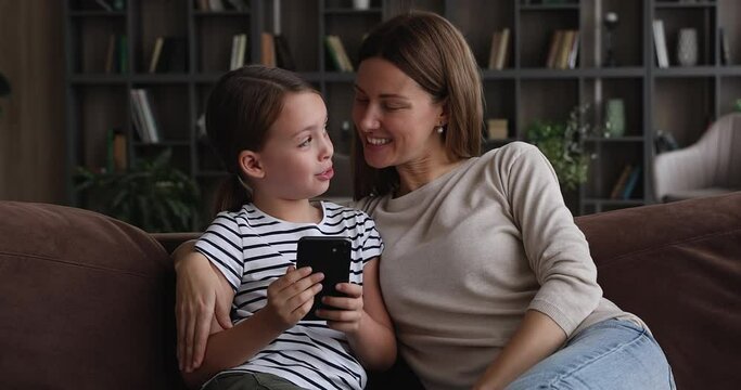 Little girl and mother spend free time use smartphone, make video call, play new online videogame. Safety of child on net, parental control. Family fun at home with children using modern tech concept