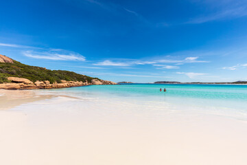 A young couple swim in the sparkling water next to the pristine white sand beach of Wharton Bay in the Cape LeGrande National Park on a clear summer day.