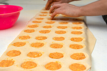 hands filling homemade pasta in sorrentino mold with ham and cheese and pumpkin filling on worktop with flour bowls and rolling pin and plastic molds