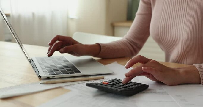 Close up view female hands use calculator laptop calculates costs working sit at table. Pay monthly bills through e-bank app. Business, summarize household expenses, manage budget, accounting concept