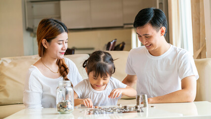 Asian family teach their daughter to saving money and putting coins into glass bank spend a quality time together. Asian family, relationship, happiness and investment concept