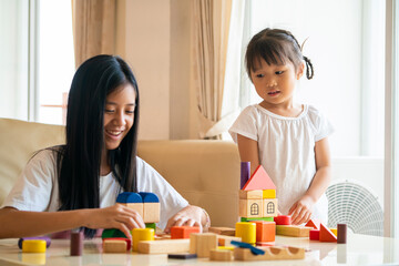 Fototapeta premium Asian girl looking at her happy mixed race sister playing wooden color block an education toy at living room. a family activity concept