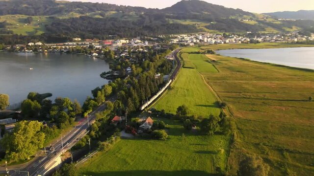 Aerial drone shot showing SBB train driving towards Rapperswil on a summer evening