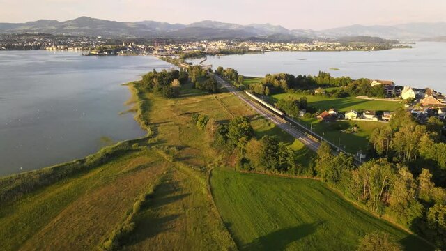 Aerial drone shot tilting up and showing SBB train driving towards Rapperswil Switzerland on a summer evening